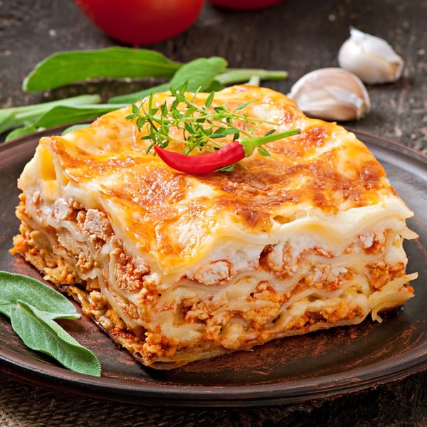A delicious slice of Roma's lasagna with rich meat sauce, cheese, and fresh herbs on a dark plate.