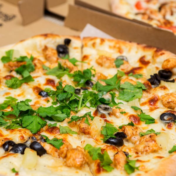 Close-up of a Roma's Pizza with chicken, black olives, pineapple, and fresh parsley.