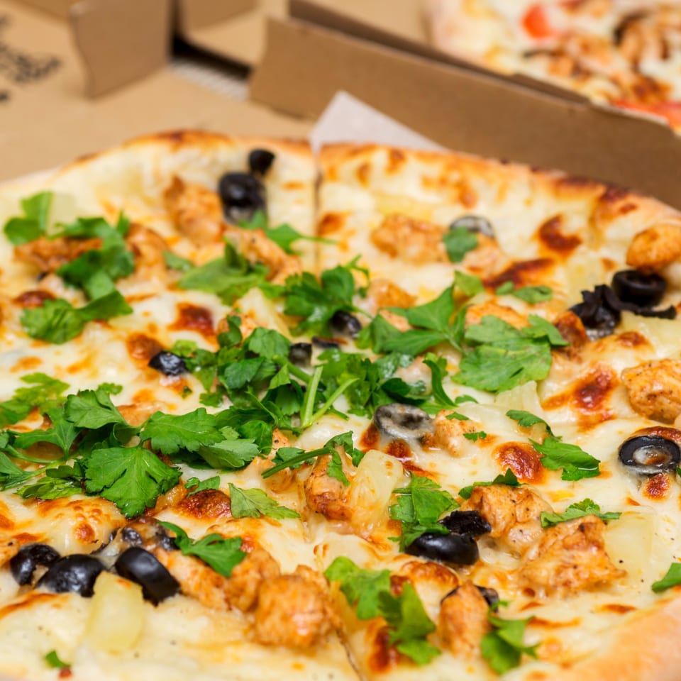 Close-up of a Roma's Pizza with chicken, black olives, pineapple, and fresh parsley.