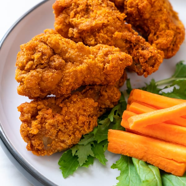 Crispy fried chicken tenders with a side of fresh green lettuce and carrot sticks on a white plate.